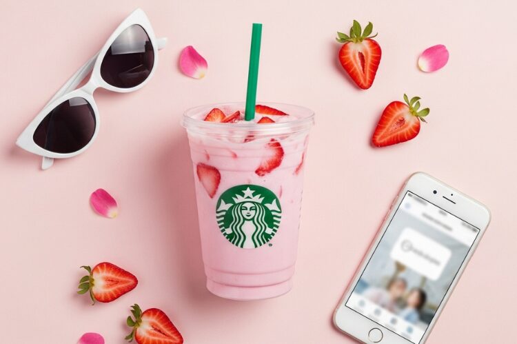A pastel pink Starbucks drink made with coconut milk and strawberries in a clear cup.