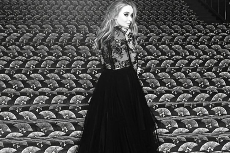 Sabrina Carpenter mid-performance wearing a sheer, feathered mini dress with fringe details.