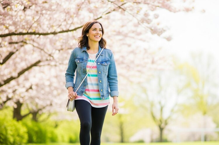 A cheerful mom on the soccer sidelines in spring weather, wearing a denim jacket, striped tee, and sneakers.