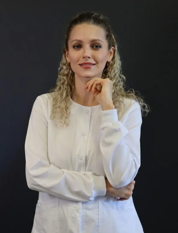 Viktoriia Shykyriava smiling in a white outfit, hand on chin, posing confidently against a dark background.