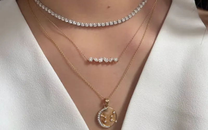 Layered gold and diamond necklaces worn with a white V-neck blouse.