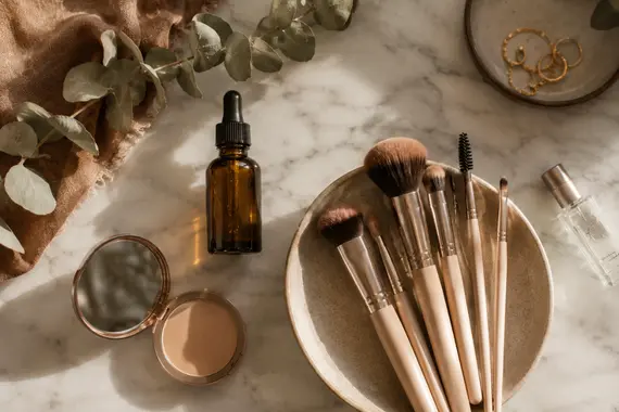 BeautyLiesTruth Picture Makeup brushes, cosmetics, skincare bottle, and compact on a marble surface.