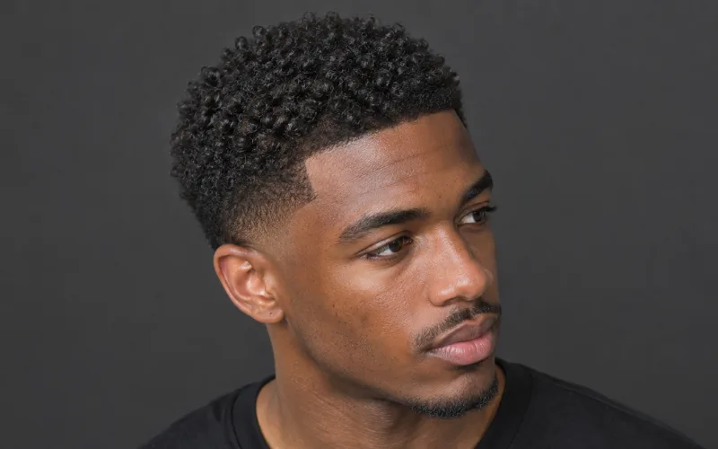 Man with short coily hair and a fade haircut against a dark background.