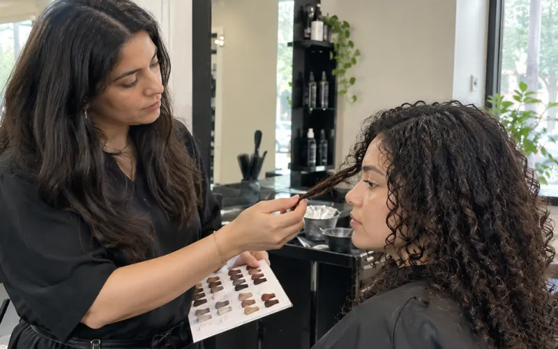 Salon stylist examining a client's curly hair with a color swatch chart.