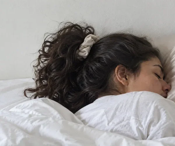 Woman sleeping on her side with long wavy hair tied in a loose pineapple, resting on a satin pillow.