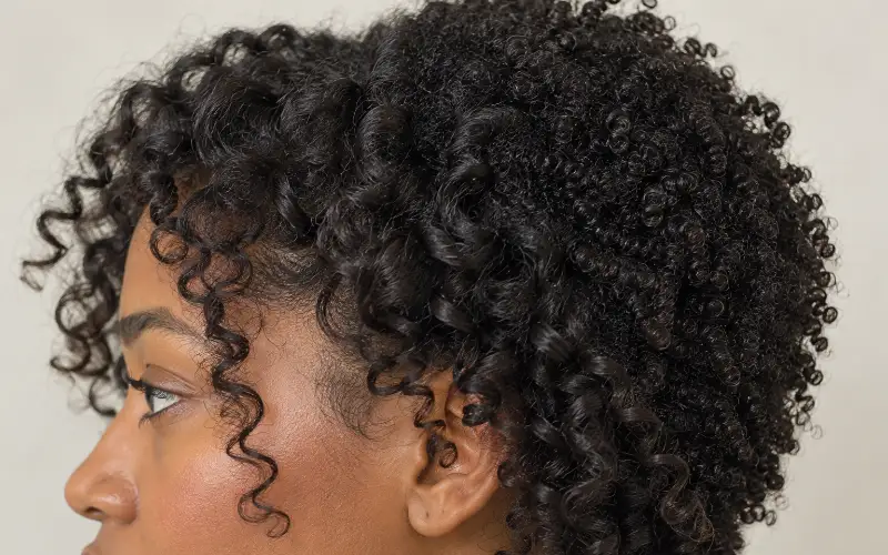 Close-up side profile of a woman's tightly coiled curly hair with defined spiral ringlets.
