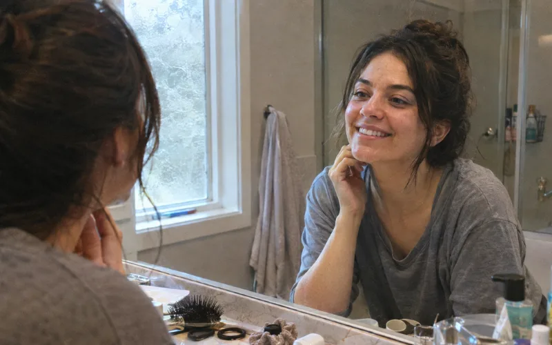 Woman smiling at her reflection in a bathroom mirror.
