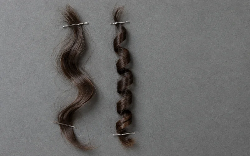 Wavy 2C hair strand next to tight 3B curl, clipped