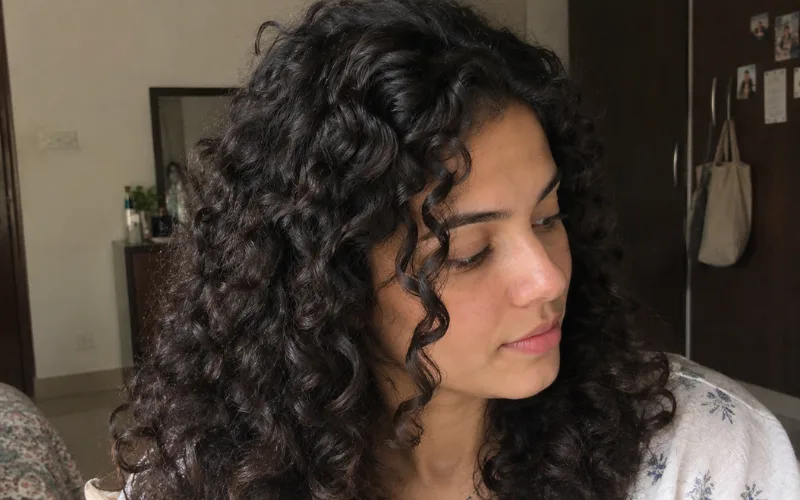 Woman with natural 3A curly hair in a realistic bedroom setting.