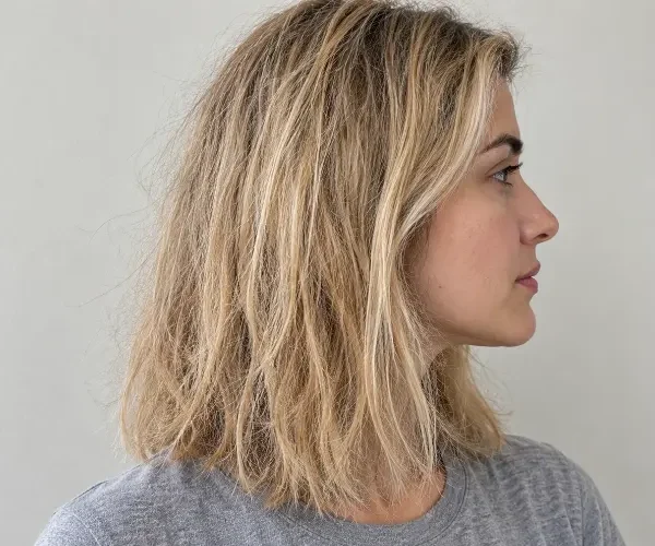 Woman with dry, frizzy blonde hair in side profile.